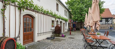 A cobblestone courtyard with outdoor seating, a barrel, and a building with arched windows and a door.