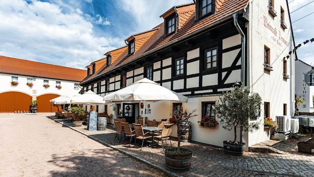 Edificio europeo tradicional con un patio, mesas al aire libre y un letrero que indica un restaurante.