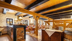 Un interior rústico con vigas de madera a la vista, una zona de bar con ladrillo y un espacio de comedor con mesas y sillas de madera.