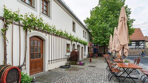 A cobblestone courtyard with outdoor seating, a barrel, and a building with arched windows and a door. - Room 'Im Weinrestaurant 6' with Shared Garden and Wi-Fi (Coswig)