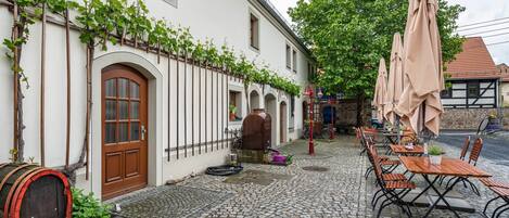 A cobblestone courtyard with outdoor seating, a barrel, and a building with arched windows and a door.