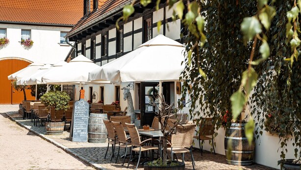 Ein Innenhof mit Außenbestuhlung, einem weißen Sonnenschirm und einem Gebäude mit Ziegeldach.
