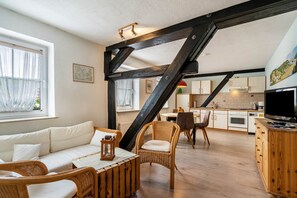 Een moderne woonkamer met een bank, stoelen, een houten eettafel en een keuken op de achtergrond.