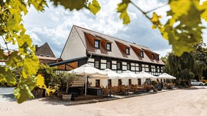 Ein traditionelles Gebäude mit einem geneigten Dach, Außenplätzen mit Sonnenschirmen und einer gepflasterten Fläche davor.
