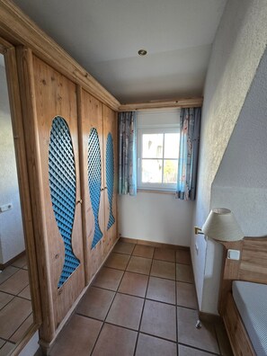 Een kamer met een houten garderobe, een raam met gordijnen, een lamp en betegelde vloeren.