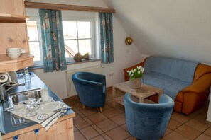 Een kleine keuken met een spoelbak, een eethoek met een blauwe stoel, een bank en een tafeltje met een vaas.