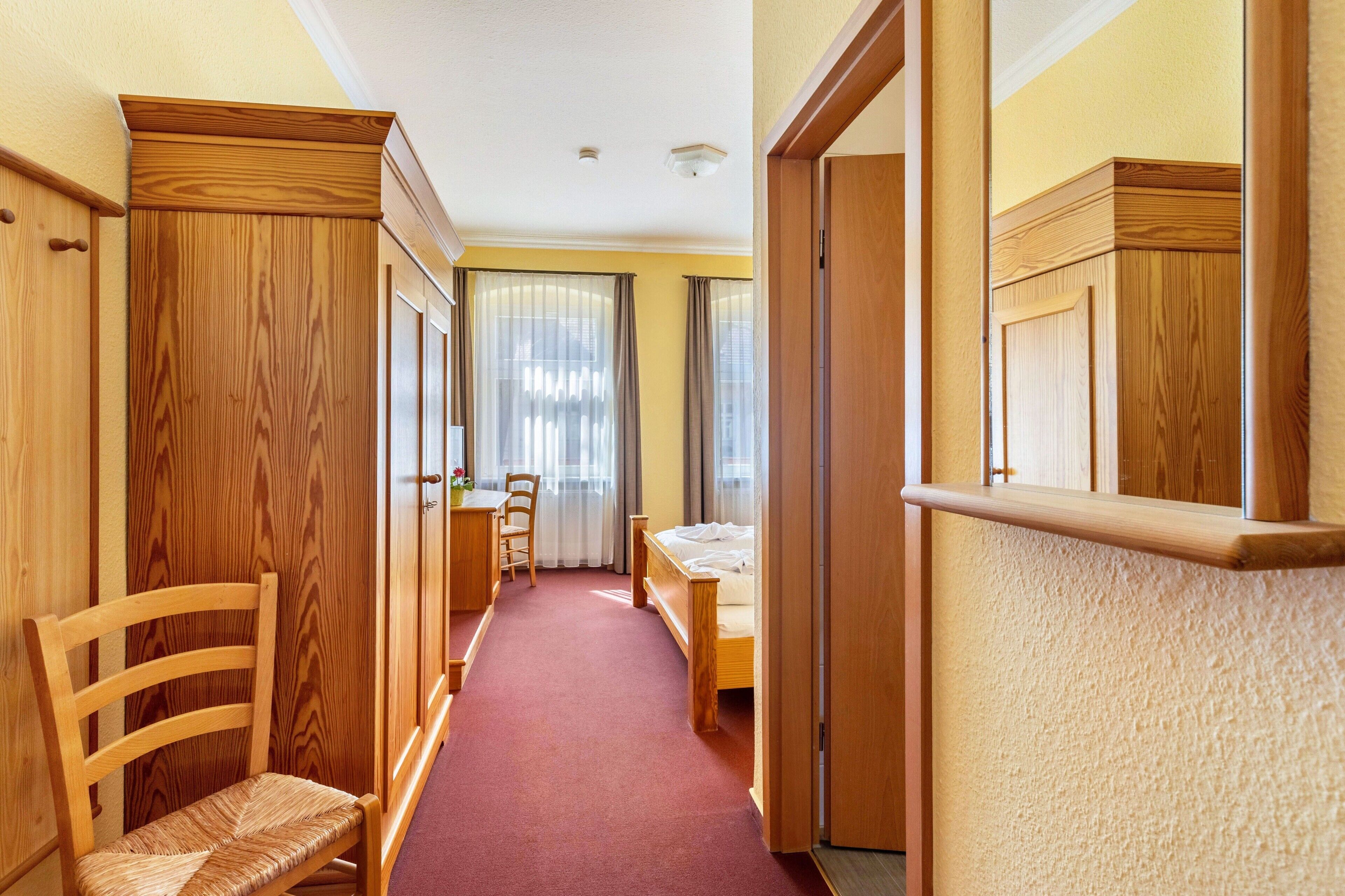 A narrow hallway with wooden walls, a bed, a desk, and a chair.