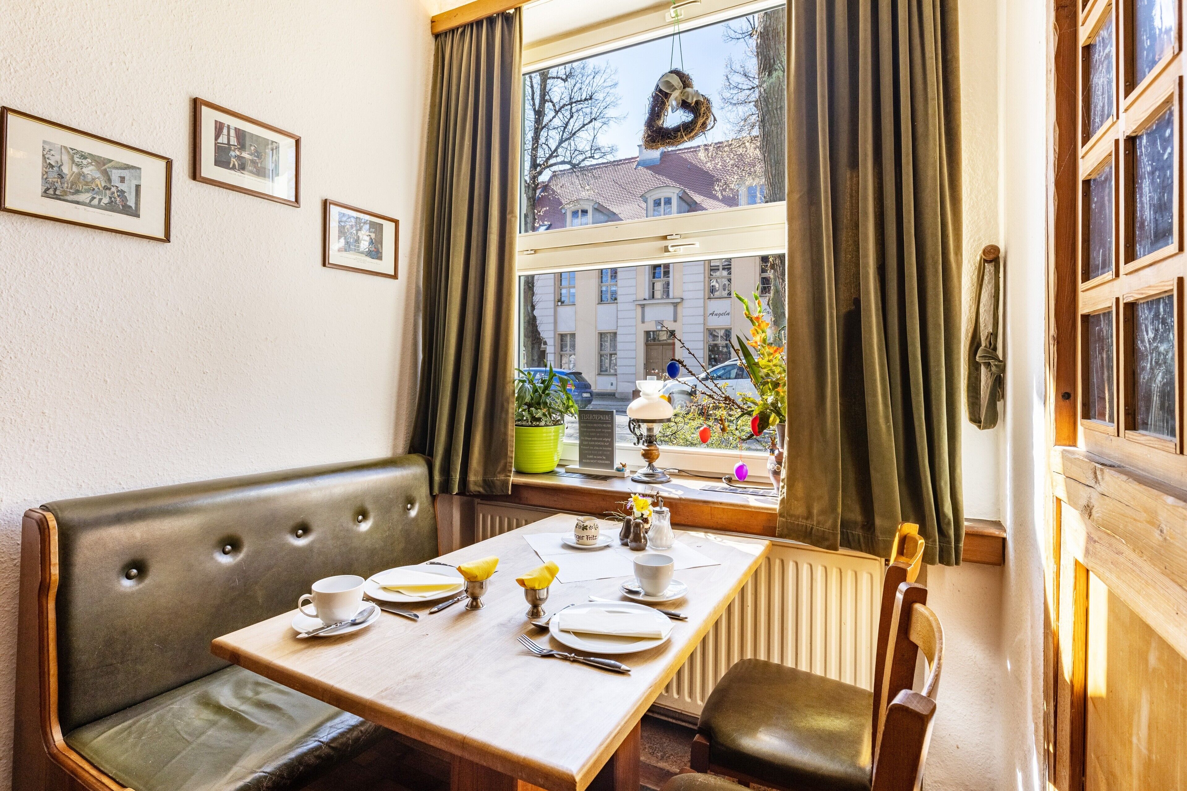 A dining area with a table set for two, a bench, and a window with curtains.