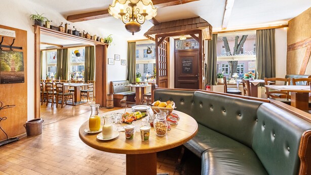 Ein gemütliches Restaurant mit Holztisch, gedecktem Frühstück und einer gepolsterten grünen Bank, sowie einer Kristallleuchter.