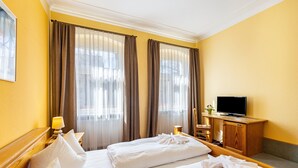 Ein Hotelzimmer mit zwei Betten, einem Fernseher, einem Holzschrank und einem Fenster mit Vorhängen.