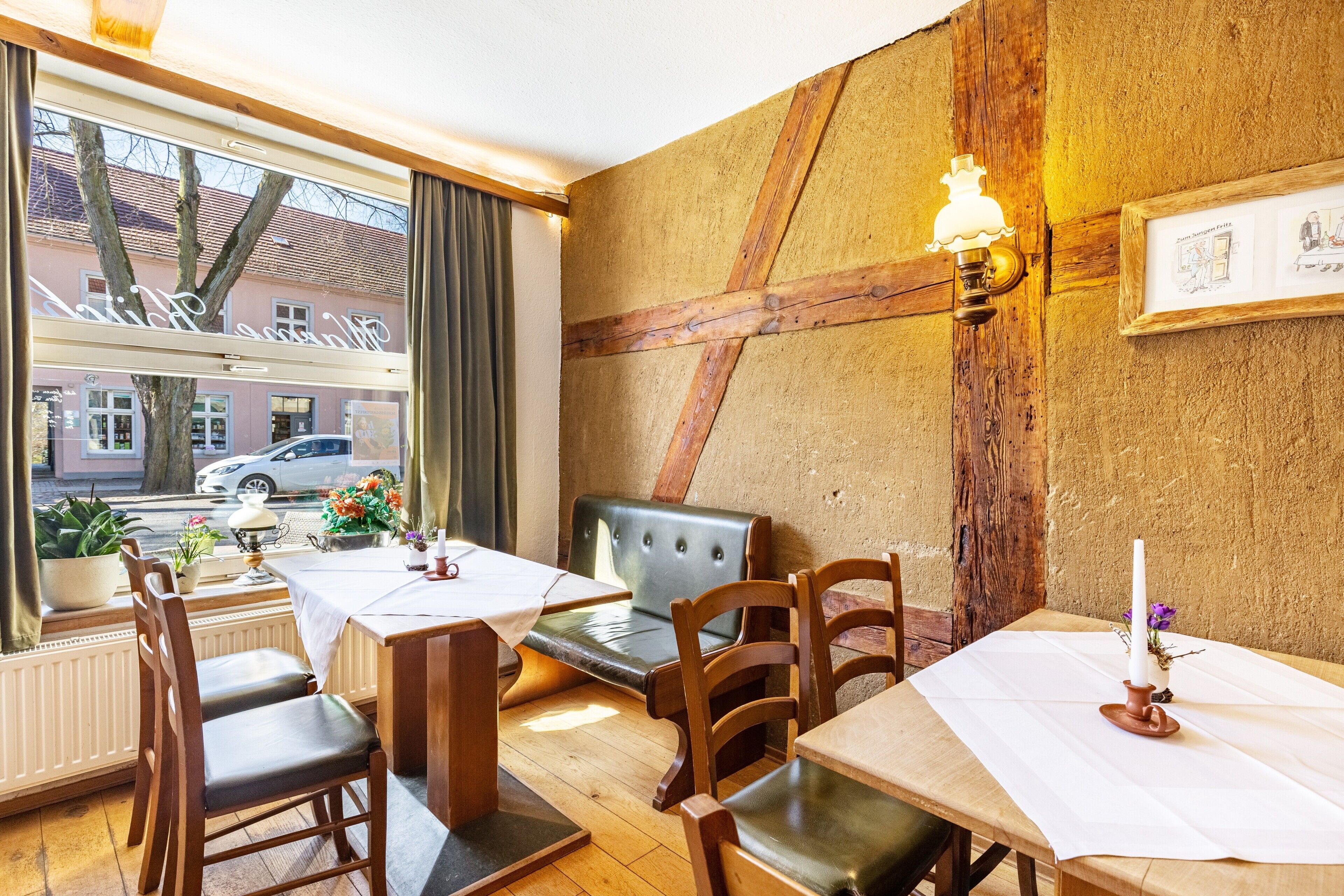 Interior de un restaurante con mobiliario de madera, un ventanal con vistas a la calle y un cuadro en la pared.