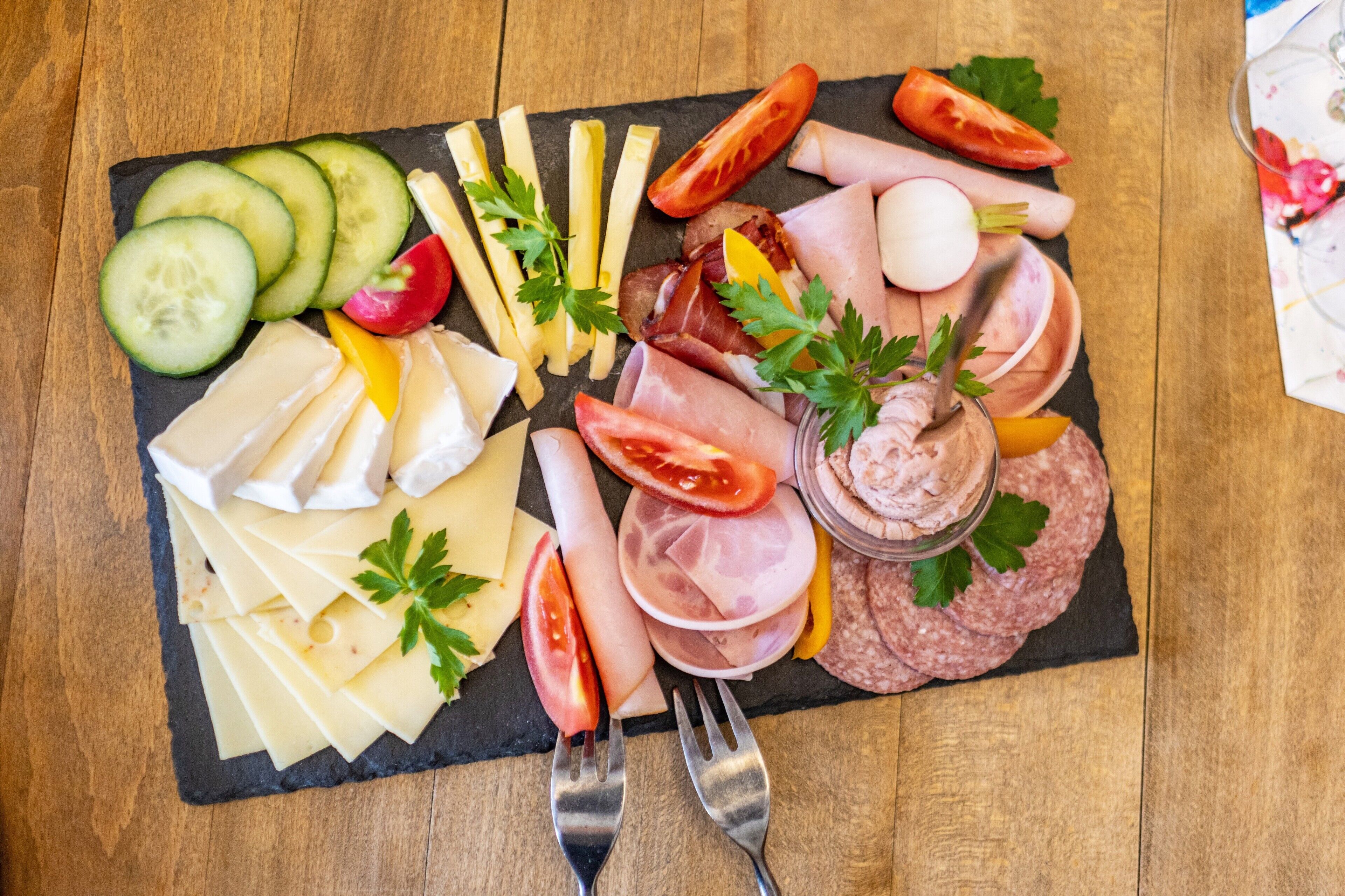 Une planche de charcuterie comprenant divers fromages, viandes et légumes, présentée sur une ardoise.