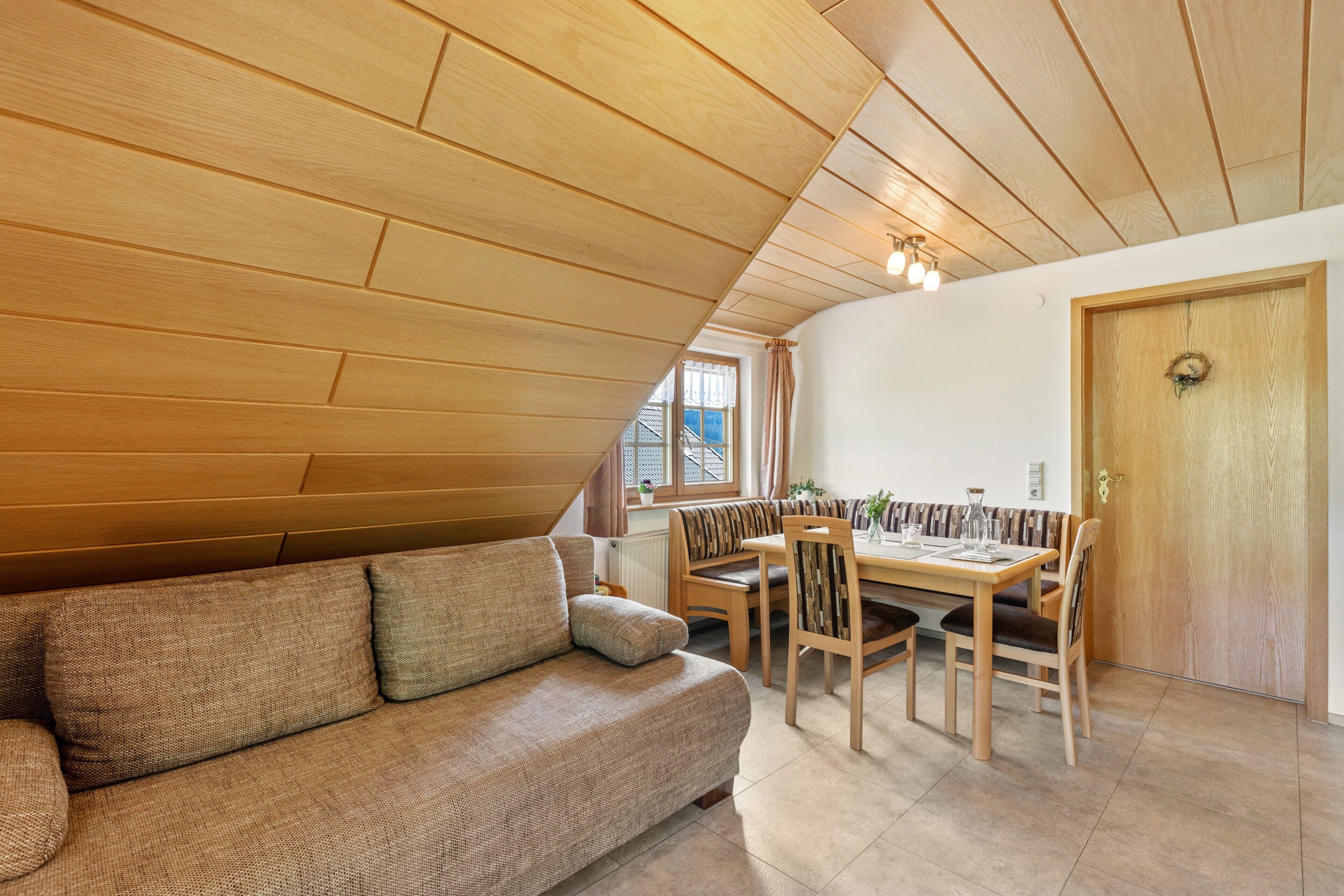 A cozy room with a wooden ceiling, a sofa, a dining table with chairs, and a door.