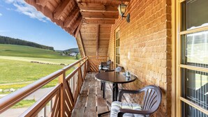 A wooden balcony with a table and chairs, overlooking a green landscape. - Attic Apartment with Mountain View, Shared Garden, and Wi-Fi (Eisenbach (Hochschwarzwald))