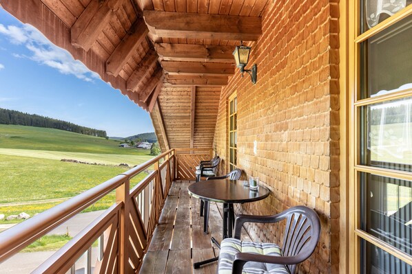 A wooden balcony with a table and chairs, overlooking a green landscape.