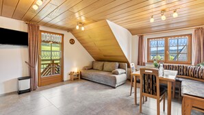 A cozy room with a sofa, dining table, and chairs, wooden ceiling, and large windows. - Attic Apartment with Mountain View, Shared Garden, and Wi-Fi (Eisenbach (Hochschwarzwald))