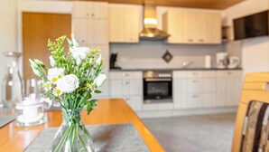 A modern kitchen with white cabinets, a stainless steel range hood, and a dining area with a table and vase of flowers. - Attic Apartment with Mountain View, Shared Garden, and Wi-Fi (Eisenbach (Hochschwarzwald))