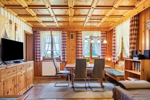 Een houten chalet inrichting met een televisie, eettafel, stoelen en een bed.
