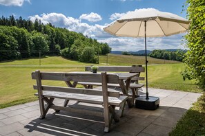 An outdoor seating area with wooden benches and a table, surrounded by a grassy field and trees. - Apartment 'Fuchsbau' with Mountain View, Private Terrace and Wi-Fi (Wolfach)