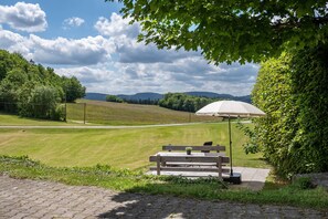 A bench with a potted plant, an umbrella, and a paved walkway in a park with a view of hills and trees. - Apartment 'Fuchsbau' with Mountain View, Private Terrace and Wi-Fi (Wolfach)