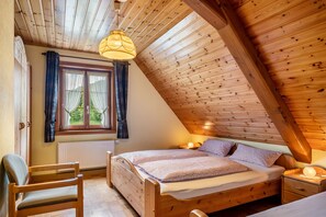 A wooden-paneled room with a bed, a chair, a window with curtains, and a hanging light fixture. - Apartment 'Fuchsbau' with Mountain View, Private Terrace and Wi-Fi (Wolfach)