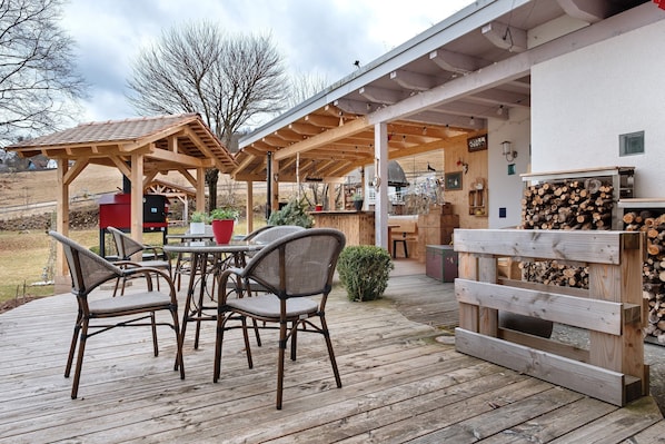 A wooden deck with outdoor seating, a barbecue area, and a stack of firewood.