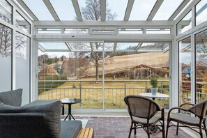 A conservatory with a glass roof, a patio with a table and chairs, and a view of a rural landscape. - Apartment 'Uwe's Stube' with Shared Terrace, Shared Garden and Wi-Fi (Lenzkirch)