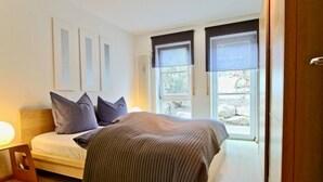 Ein Schlafzimmer mit einem Bett, einem Nachttisch, einem Fenster mit Jalousien und einer Tür.