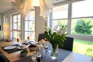 A dining table set with plates, cups, a vase of flowers, and a bowl of fruit. - Apartment 'Am See' with Private Terrace, Shared Garden and Wi-Fi (Bodman-Ludwigshafen)