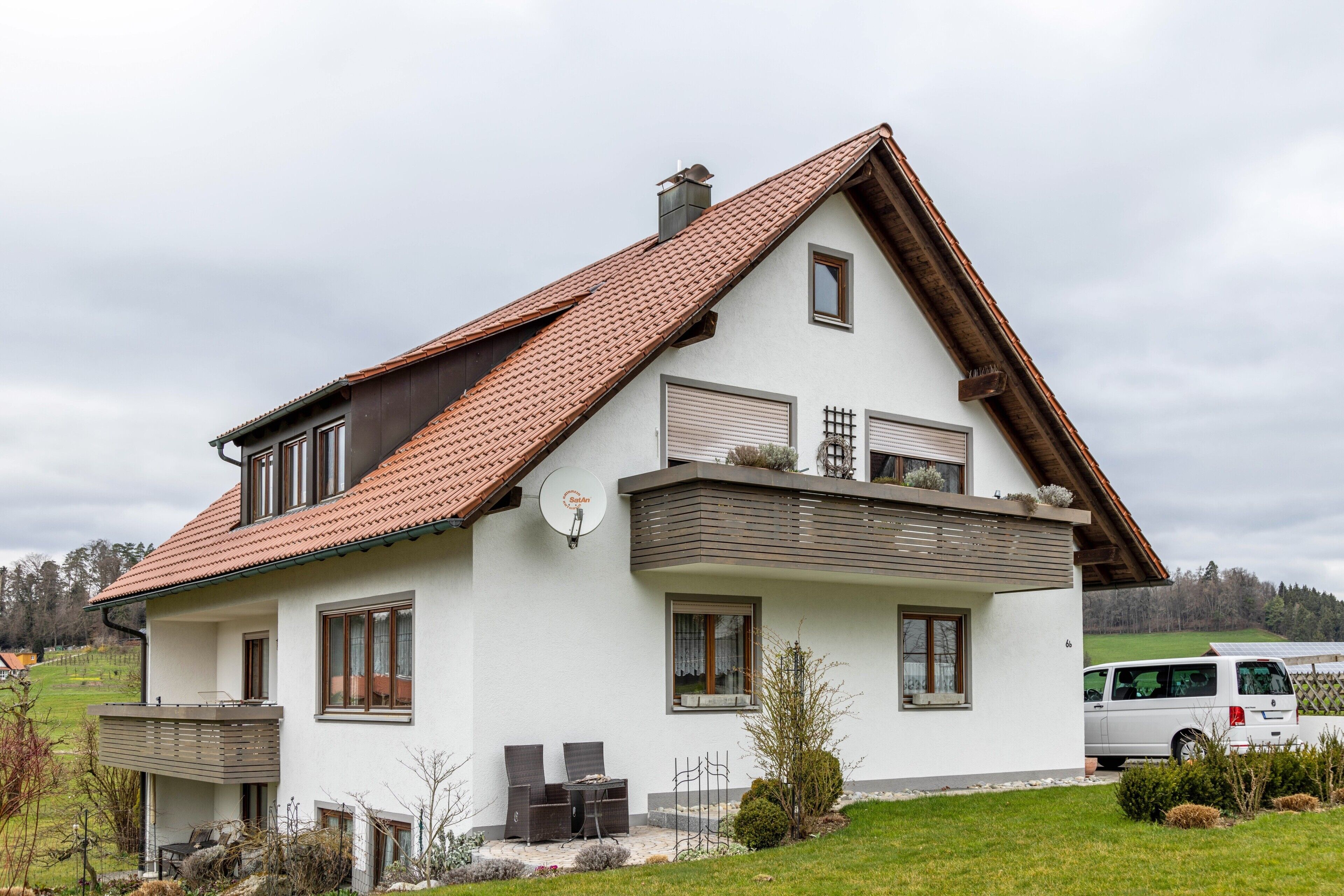 A two-story house with a sloped roof, a balcony, and a satellite dish.