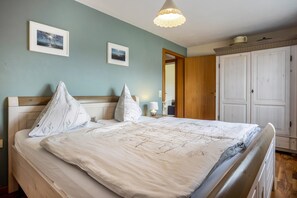 A neatly made bed with a white and gray patterned bedspread, a wooden headboard, and two wall-mounted pictures.