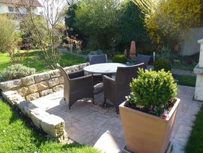 Une terrasse avec une table ronde et des chaises en osier, entourée d’un mur de pierre et de verdure.