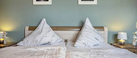 A double bed with a leaf-patterned duvet, two bedside tables with lamps, and two framed pictures on the wall.
