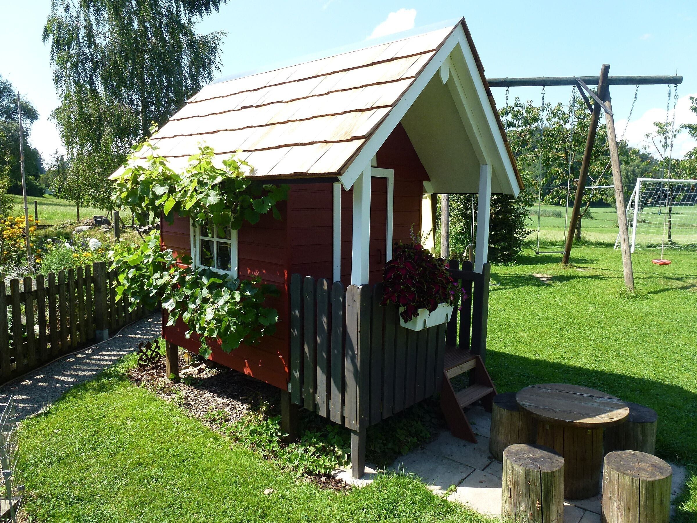 A small red wooden structure with a porch, a window, and a planter box.