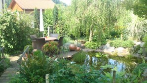 A garden with a pond, wooden deck, and outdoor furniture.