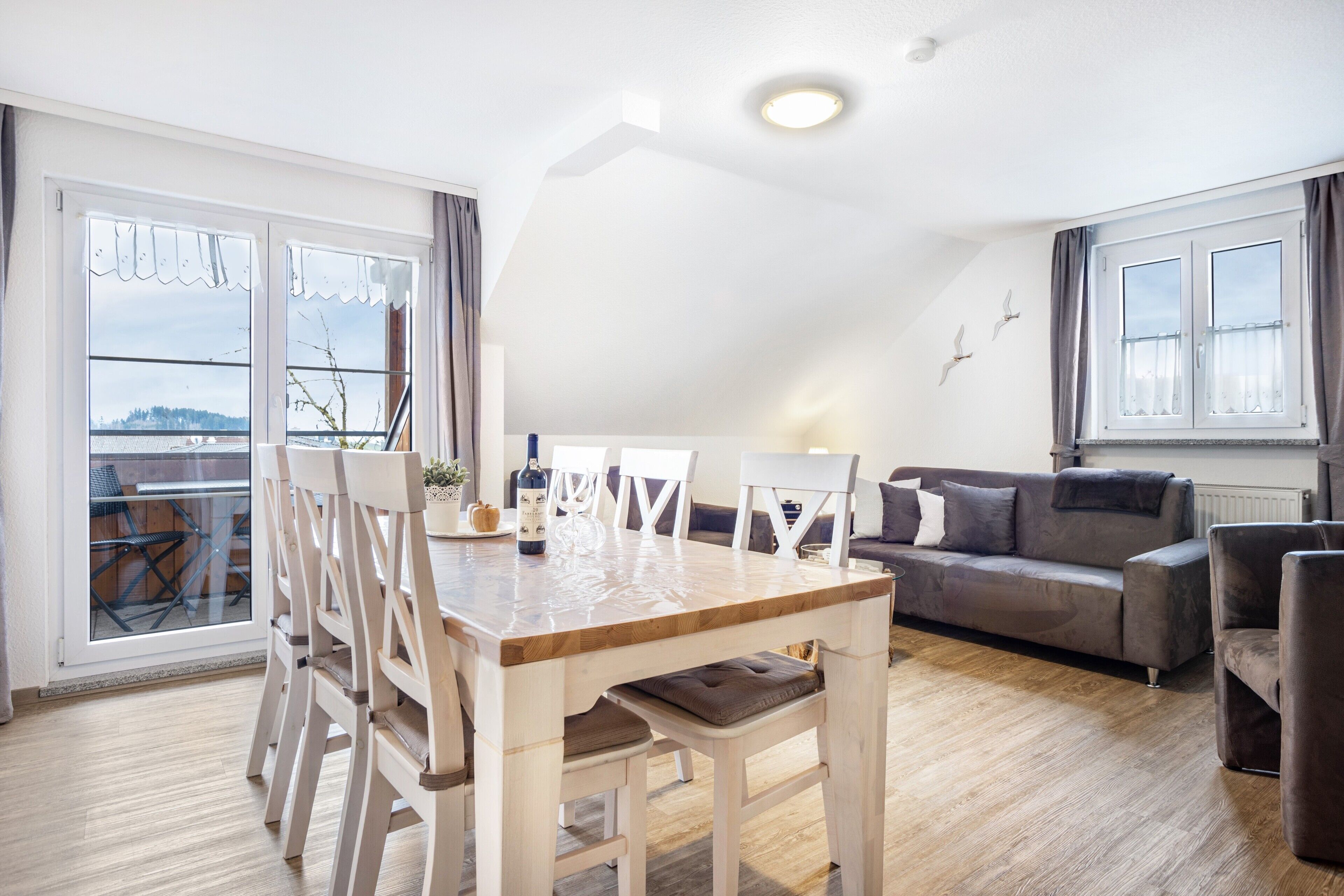 Un salon moderne avec une table à manger, des chaises blanches, un canapé gris et un balcon avec vue.