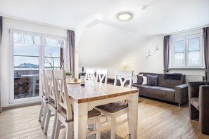 A modern living room with a dining table, white chairs, a grey sofa, and a balcony with a view.