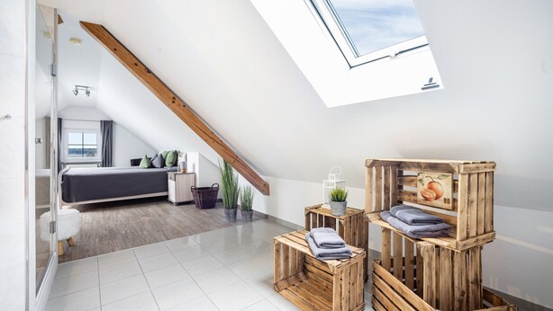 A modern loft bedroom with a skylight, a bed, a small seating area, and a wooden crate storage unit.
