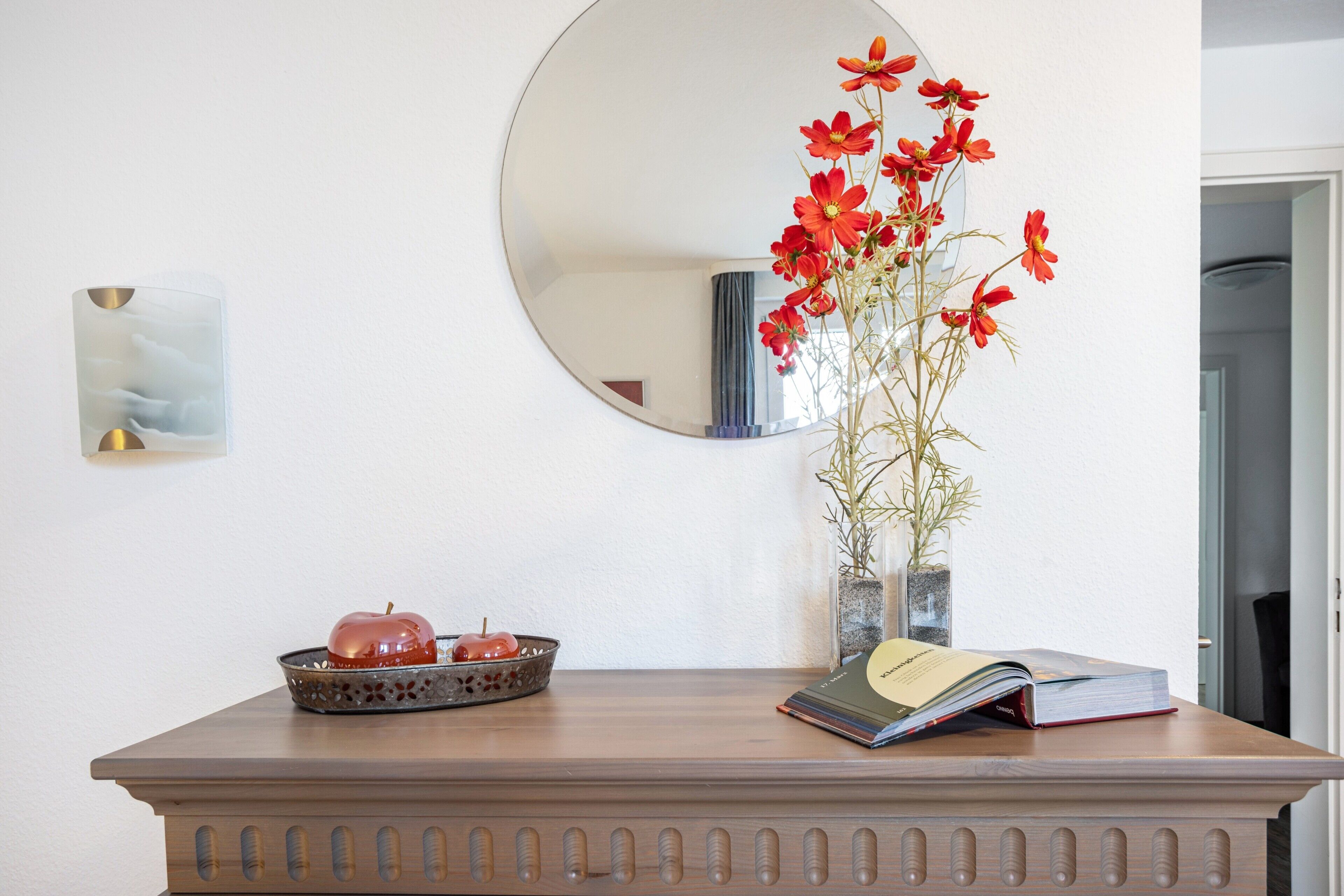 Ein Holztisch mit einer dekorativen Schale, einem roten Apfel, einem Buch und einer Vase mit Blumen.