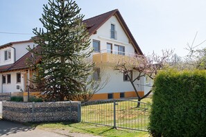 A two-story house with a stone wall, a metal fence, and a large tree in the foreground.