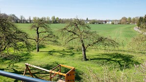 Un paysage rural avec un ciel dégagé, des champs verdoyants et une structure en bois au premier plan.