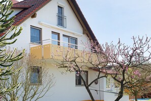 A two-story house with a balcony, windows, and a tree with pink blossoms.