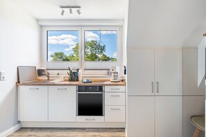 Een moderne keuken met een ingebouwde oven, een koffiezetapparaat en een raam met uitzicht op bomen.