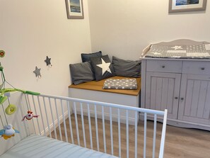 A baby room with a crib, a wooden bench with pillows, a cabinet, and wall decorations. - Apartment 'Ferienwohnung Ankerleicht' with Shared Terrace, Shared Garden and Wi-Fi (Steinbergkirche)