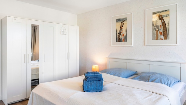 Een slaapkamer met een bed, een kledingkast en twee kunstwerken in lijsten aan de muur.