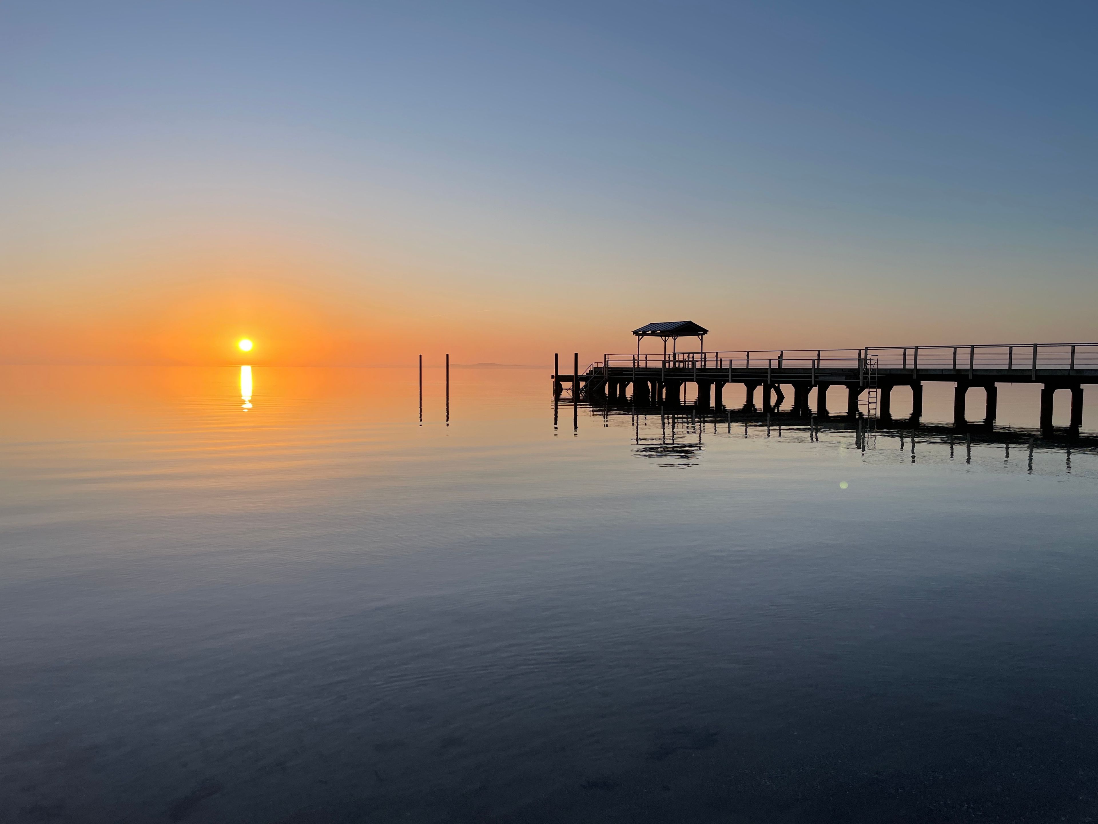A pier extending into calm water with a clear sky.