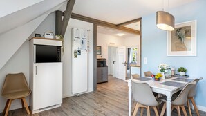 Eine moderne Küche mit integriertem Kühlschrank, ein Essbereich mit Tisch und Stühlen sowie eine Treppe, die zu einer oberen Ebene führt.