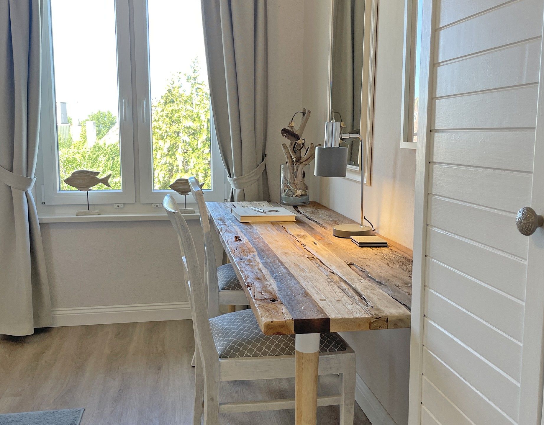 A wooden dining table with chairs, a vase with dried branches, and a lamp.