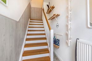 A staircase with wooden steps and white walls, leading to a landing with a white radiator and a wall-mounted rack.