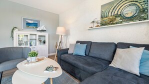 Een moderne woonkamer met een grijze bank, een witte salontafel en een schilderij van een landschap.